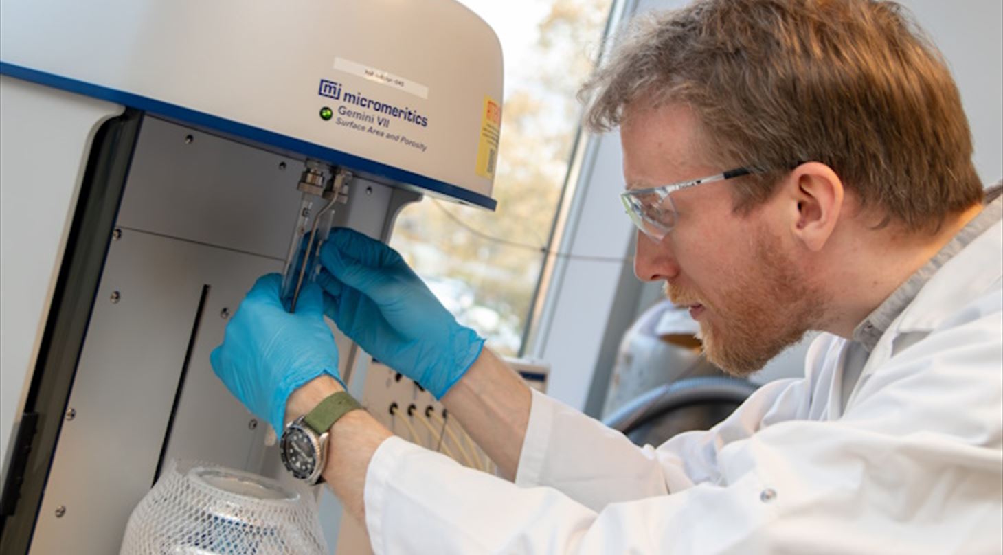 Man in lab coat placing a chemical sample in an analysis equipment.